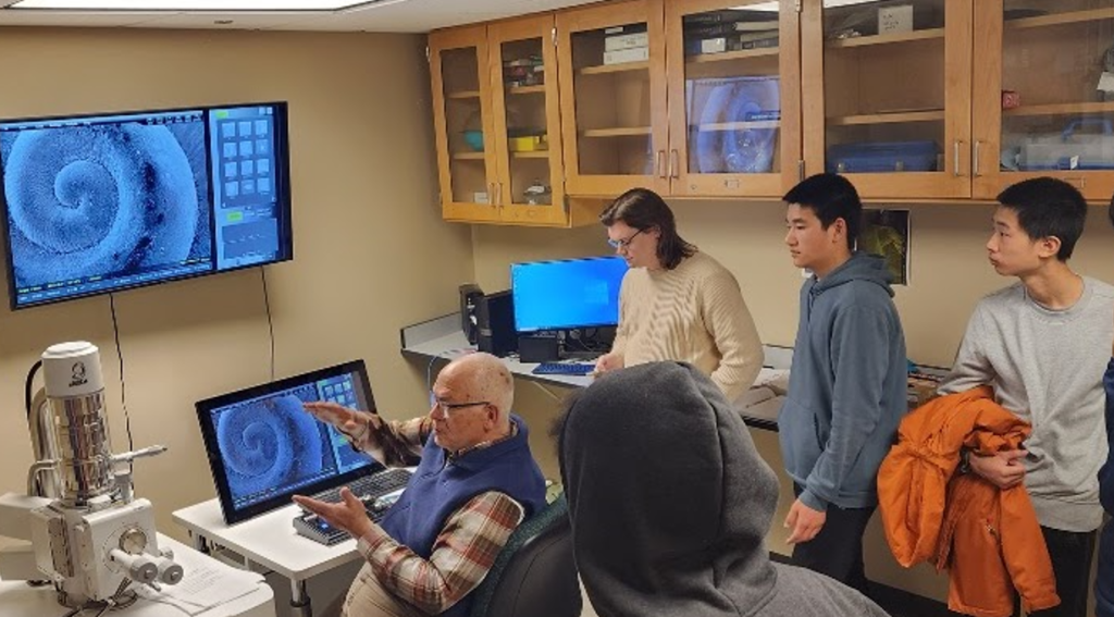 High school students looking at computer in laboratory with professor